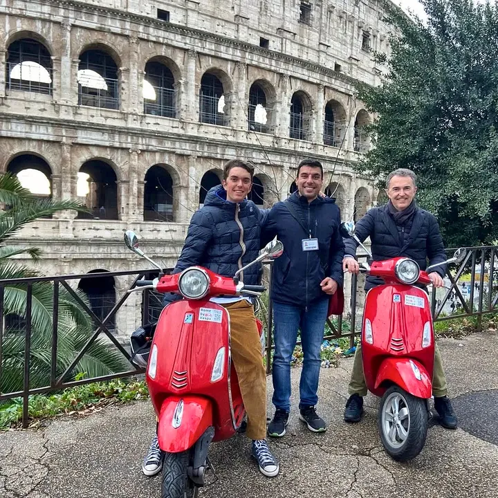 Guide and two guests with red Vespas in front of the Colosseum