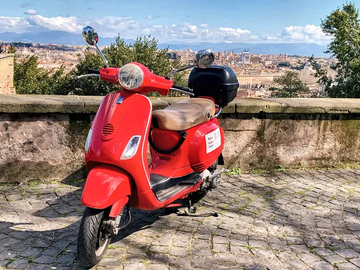 A red Vespa with the Rome skyline behind it