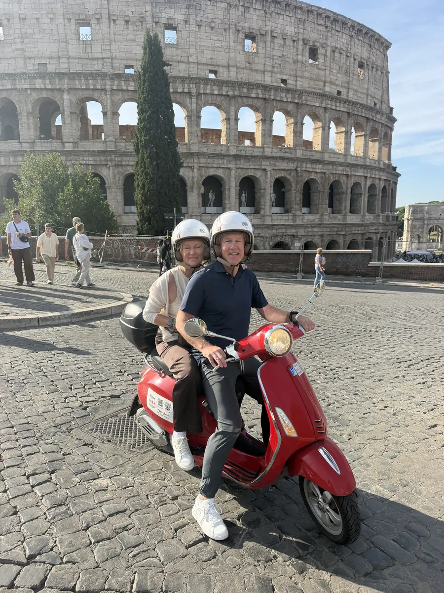 A couple on a red Vespa in front of the Colosseum