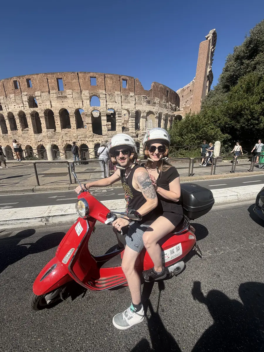 Two riders on their own Vespa beside the Colosseum