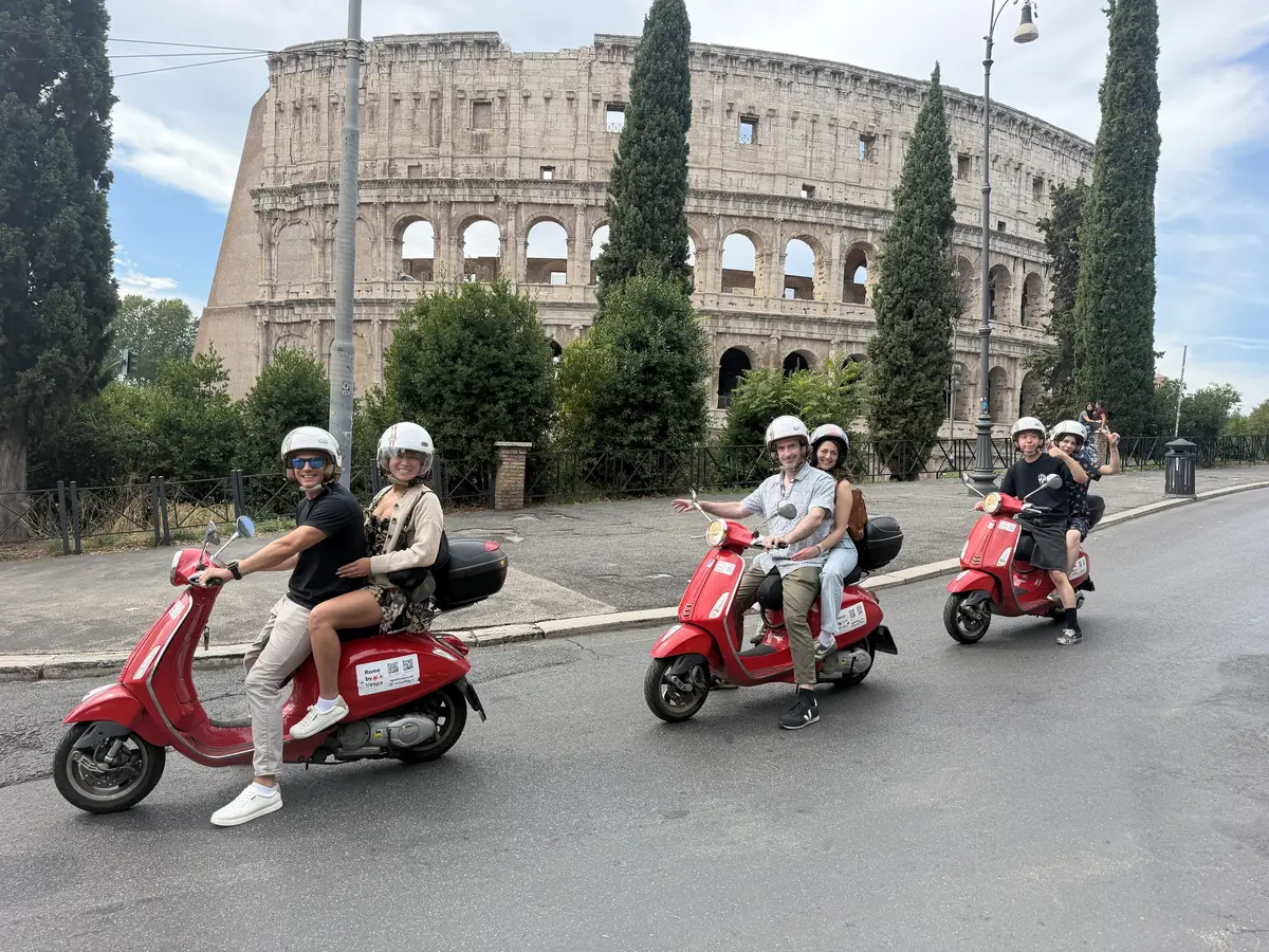 Three couples on red Vespas in front of the Colosseum