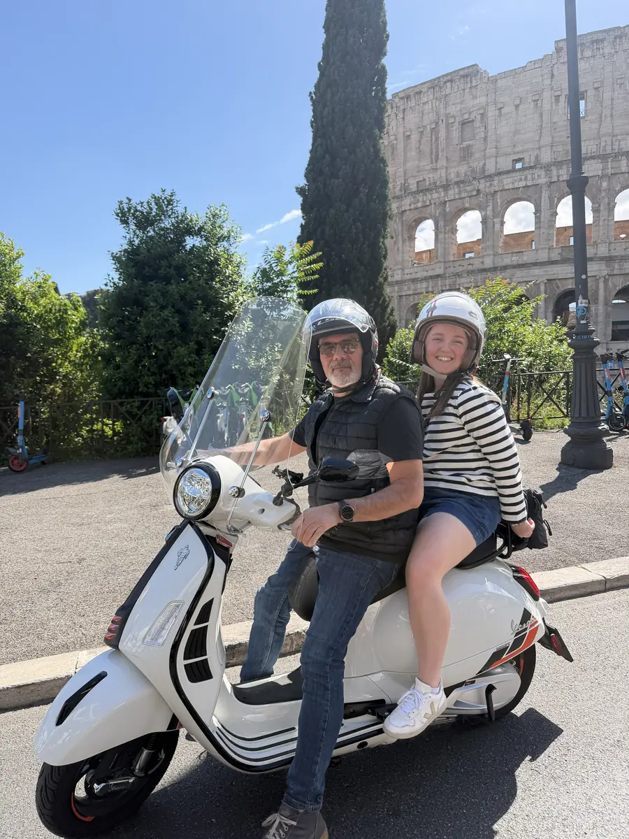 A guest riding as a passenger on a white Vespa at the Colosseum